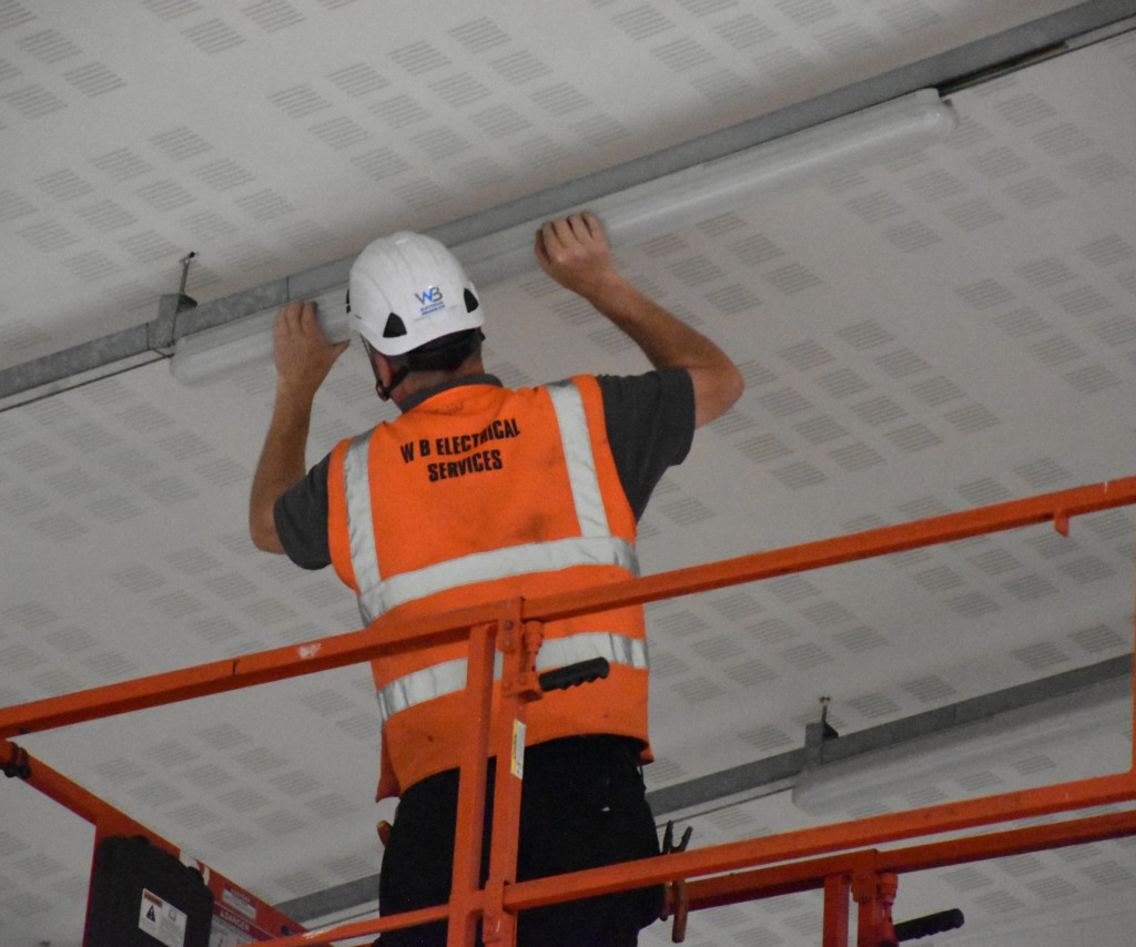 Engineer testing warehouse lighting during planned maintenance inspection