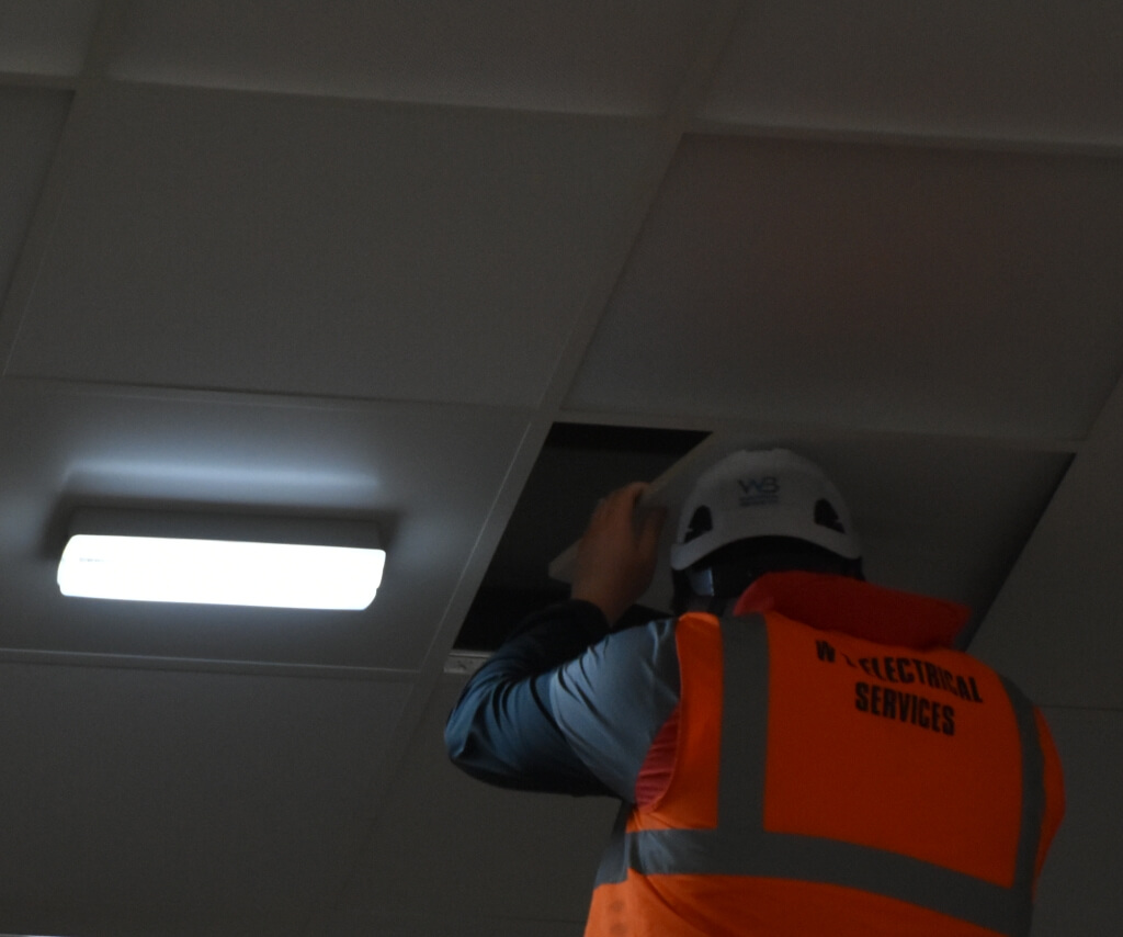 WB Electrical engineer installing LED ceiling panel light during an office lighting upgrade